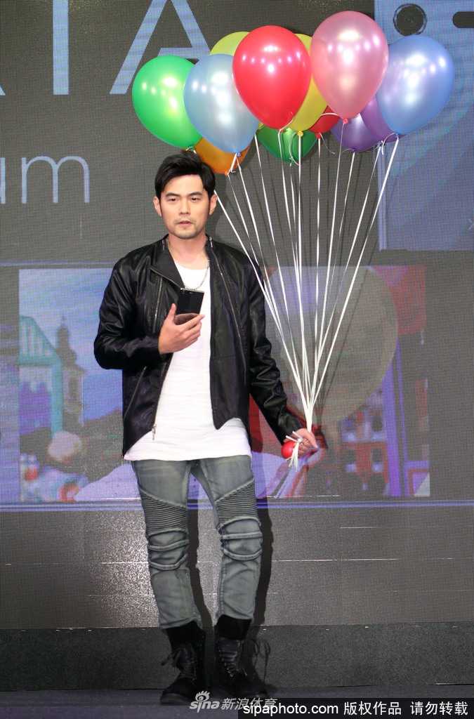 周杰伦拿起手机自拍，镜头前的他眼神专注，背景是模糊的活动灯光，仿佛要将这一刻的欢乐全部收录。