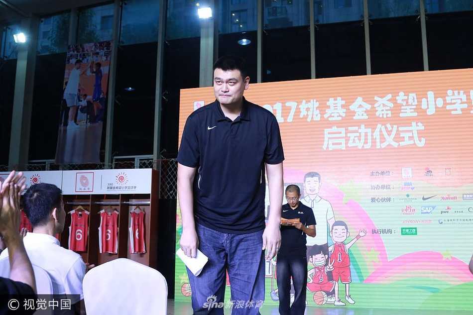 姚明双手稳稳托住一面印有姚基金标志的蓝色旗帜，神情庄重地将它授予南京市的代表，旗帜在微风中轻轻展开，象征着责任与梦想的传递，也预示着今年夏天的全国赛将正式落户古都南京。