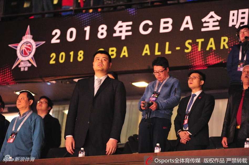 姚明端坐在看台上，双手轻轻搭在膝盖，嘴角不自觉地上扬，露出憨厚而专注的“姨母笑”，眼神里满是对后辈的关爱。