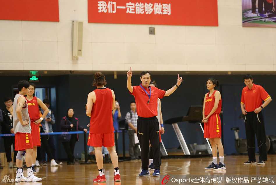 女篮主帅许利民亲自上阵，弯下腰为队员做防守示范，眼神中透露出严师的犀利与期待，他的肢体语言充满力量，仿佛要将自己的经验直接传递给场上的每一位球员。