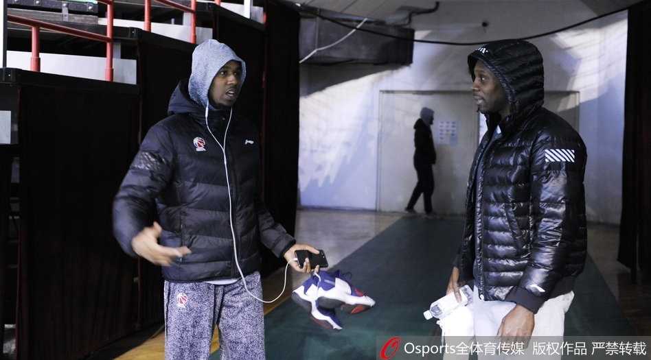 训练场上，两人并肩站立，神情专注地看向场地中央。他们穿着各自球队的训练服，在灯光的照射下，身影显得格外修长。