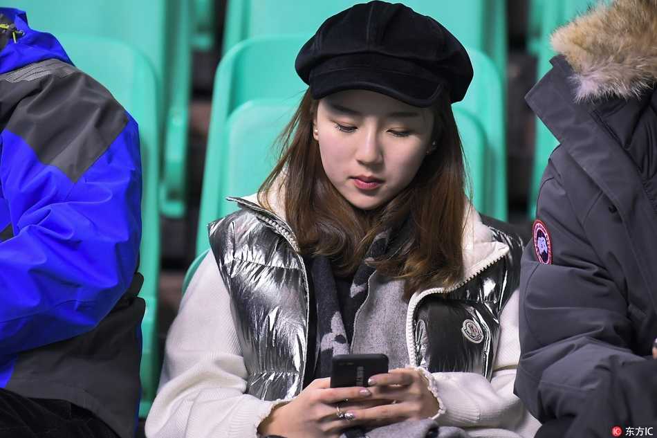 两位闺蜜球迷手持辽宁男篮的助威围巾，脸颊上贴着闪亮的球队贴纸，在喧闹的看台上窃窃私语，分享着对今晚大胜的期待。