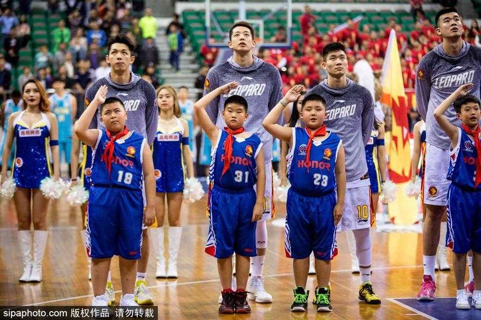 比赛间隙，一名身穿红色上衣的篮球少年在家长或教练的陪伴下，站在场边背景板前，好奇地打量着这个巨大的赛场，仿佛在丈量自己与梦想之间的距离。