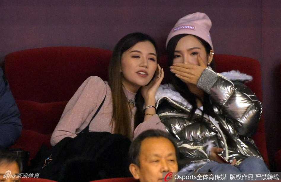 睢冉妻子举起手机对着场内拍照，想要捕捉丈夫在替补席的画面，一旁的丁彦雨航女友也侧身探头，两人共同关注着山东队的每一次攻防。