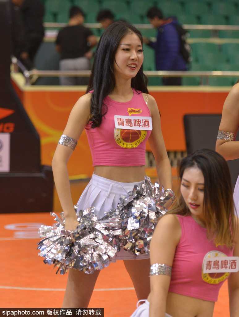 在合影的队伍中，这位扎着高马尾的宝贝笑靥如花，她微微侧身，展现出优美的身姿。白色的短裙在球馆的灯光下显得格外纯净，与伙伴们的红色上衣构成了最亮眼的色彩组合。