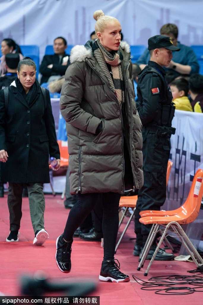 比赛间隙，这位四川女篮的外援神情放松地与同伴交流，她身着便装坐在看台上，仿佛一位普通的资深球迷，享受着现场热烈的篮球氛围。