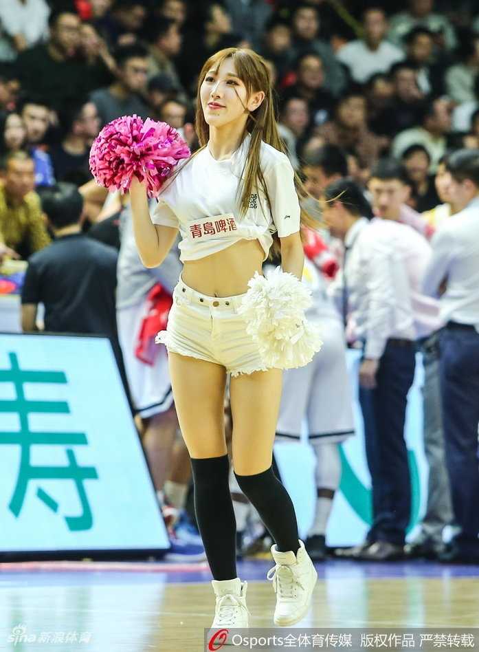 马尾辫啦啦队员回眸露出甜美微笑，背景中广厦球员正在热身，刚柔并济的画面定格了赛场内外的和谐共处。