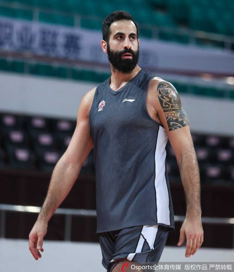 广州队球员在助教的协助下进行赛前拉伸，球员表情专注，身体线条舒展，身后的队标清晰可见，备战氛围专业而有序。