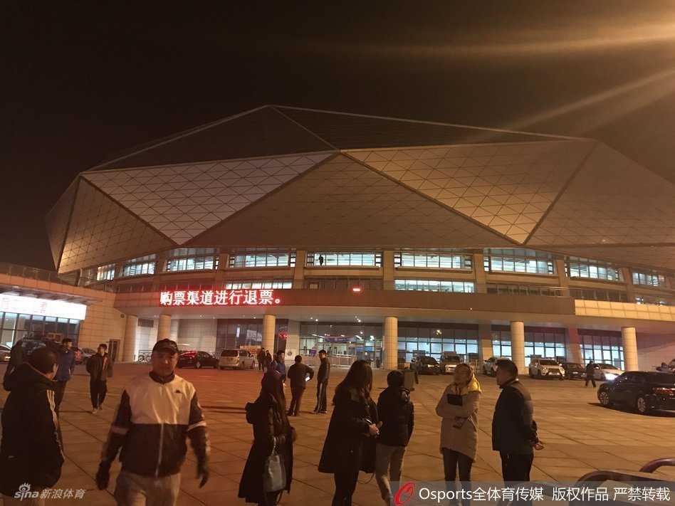 体育馆入口的玻璃门上，贴着一张临时打印的白色A4纸通知，上面清晰地写着关于本场比赛因故改期的告示和退票指引，透过玻璃门能看到馆内仍然灯火通明，却无人入场。