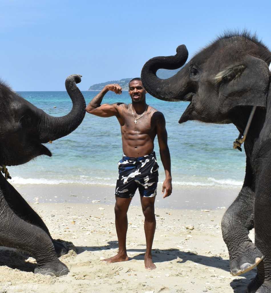 亚当斯身着深色休闲外套，在度假地点悠闲漫步，脸上带着惬意的微笑，眼神中透露出对眼前景色的欣赏，与赛场上的严肃形象形成鲜明反差。