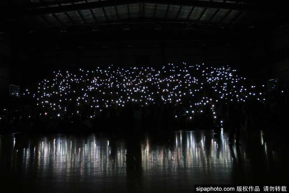 体育馆全景图，看台上布满了星星点点的手机光芒，如同银河倾泻，与球场上站立的人影构成一幅充满温情与力量的画面