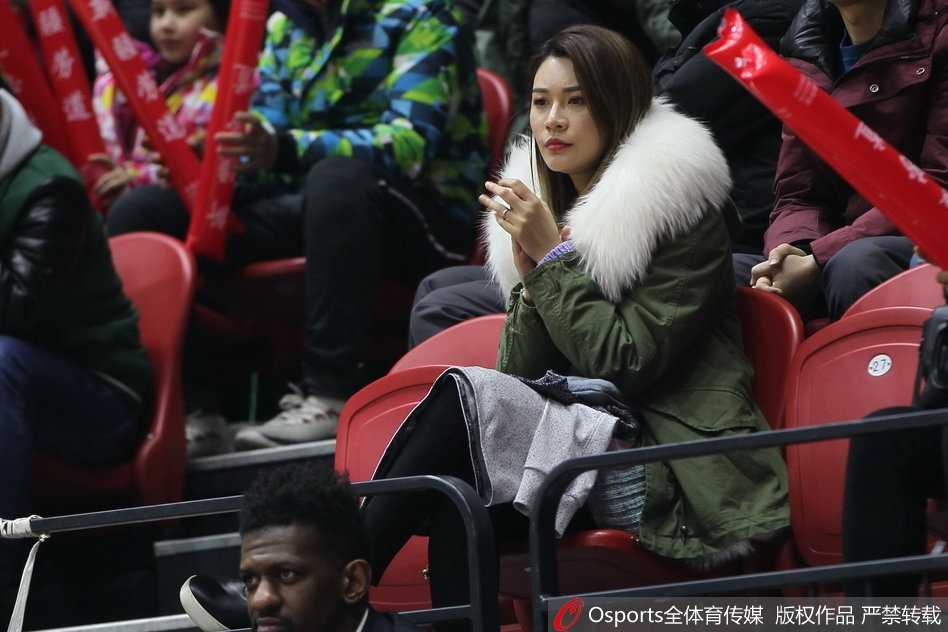 李根妻子在场边举起手机拍摄场内画面，脸上洋溢着笑容记录丈夫的赛场英姿