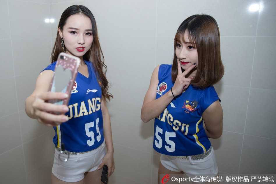 江苏肯帝亚篮球宝贝KDancer成员身穿靓丽短裙，在更衣室的柔光下回眸一笑，甜美的笑容与修长的身姿瞬间定格，为即将到来的激战注入温柔力量。