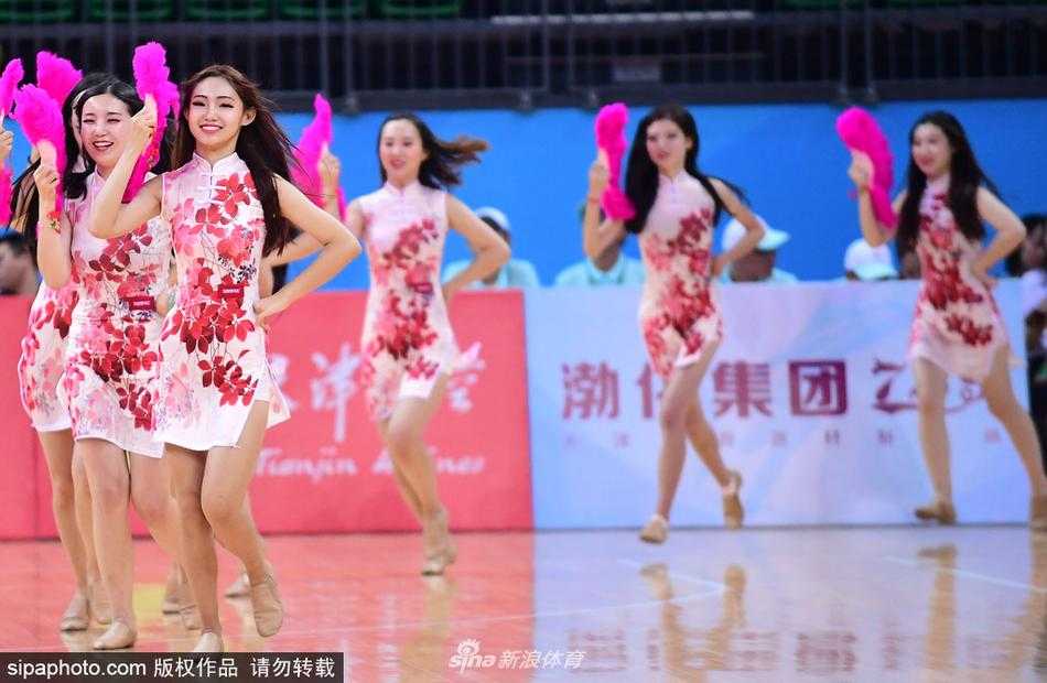 几位身着水墨晕染风格旗袍的宝贝们面带灿烂笑容，在球场中央排开舞步，裙摆随着动作轻盈飘动，与身后巨幅国旗背景相得益彰。