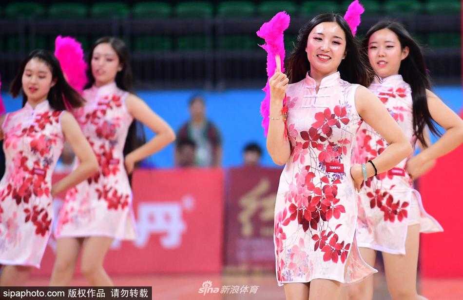 一名旗袍宝贝正做出一个托举动作，她身上的旗袍绣着精致的盘扣，在聚光灯下丝质面料泛着柔和光泽，展现了力量与柔美的完美结合。