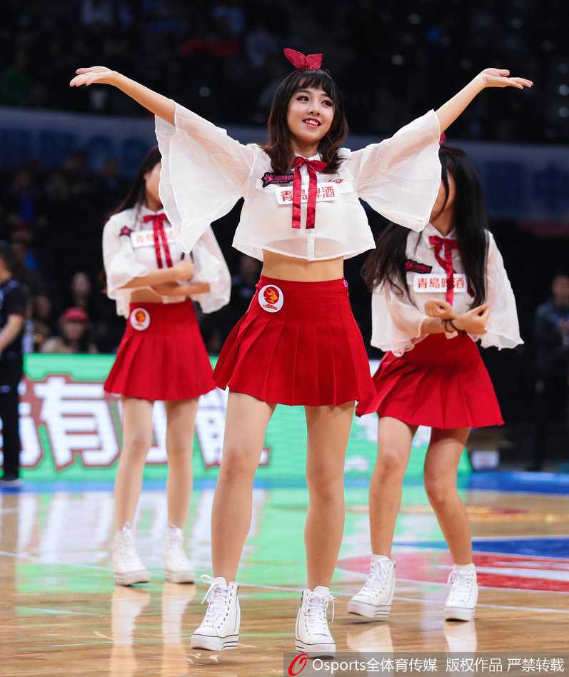 表演中的篮球宝贝们动作整齐划一，她们高高跃起，红色裙摆在空中飞扬，展现出青春洋溢的动感与活力，背景是模糊的赛场看台。