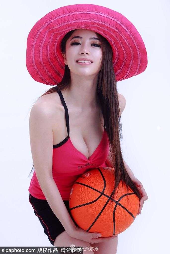 袁颖芬双手抱球置于腰间，站立在球场中央，背景虚化的看台让焦点完全集中在她自信的笑容上