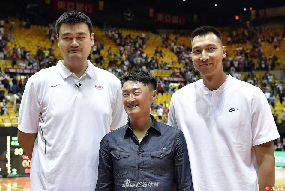 姚明与卡特面对面站着，两人脸上都洋溢着老友重逢的灿烂笑容，卡特用手指着自己下巴的胡须，似乎在与姚明分享着关于时光的趣事，身后喧嚣的球场成了他们叙旧的温馨背景。