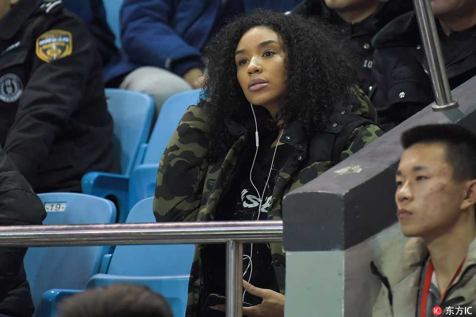 韦弗的妻子全神贯注地凝视着赛场方向，周围球迷的喧嚣仿佛与她隔绝，此刻她的心中只有对爱人最纯粹的支持，那一抹鲜艳的围巾恰如她火热的内心。