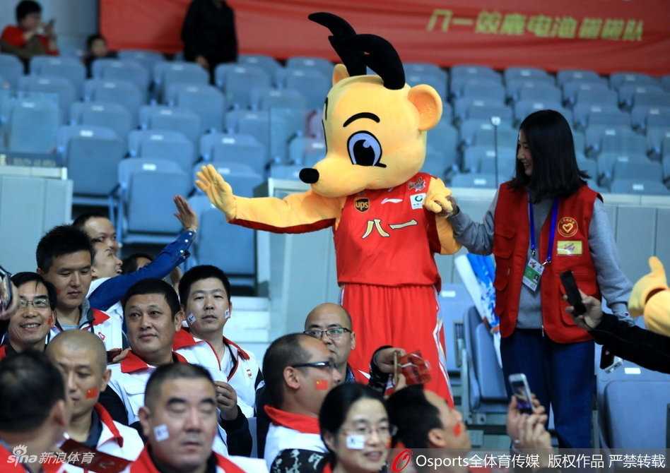 八一火箭吉祥物张开双臂与看台前排的小球迷击掌，巨大的火箭头套在灯光下显得格外亮眼，孩子们兴奋地伸出小手，场面温馨又热闹