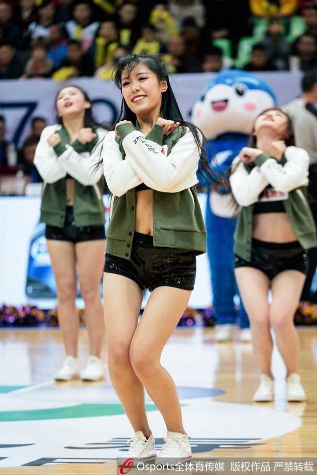 纵排构图下，一名篮球宝贝背对镜头，但依然能感受到她随着节奏扭动的身姿，华丽的服饰下摆飞扬，场边的广告牌和观众席虚化成背景。