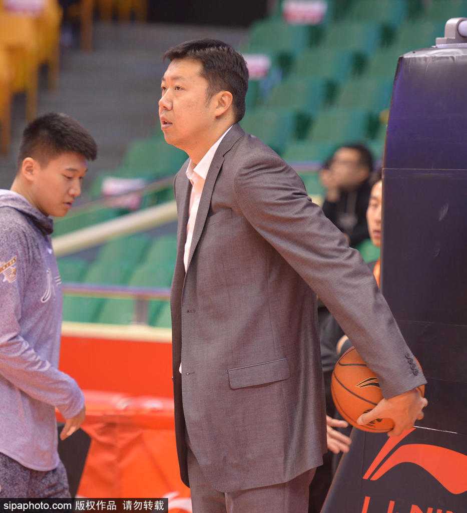 王治郅侧身低头与身边身穿西装的教练组成员交流，他神情专注，似乎在探讨即将开始的比赛战术，或是询问年轻队员的近况。