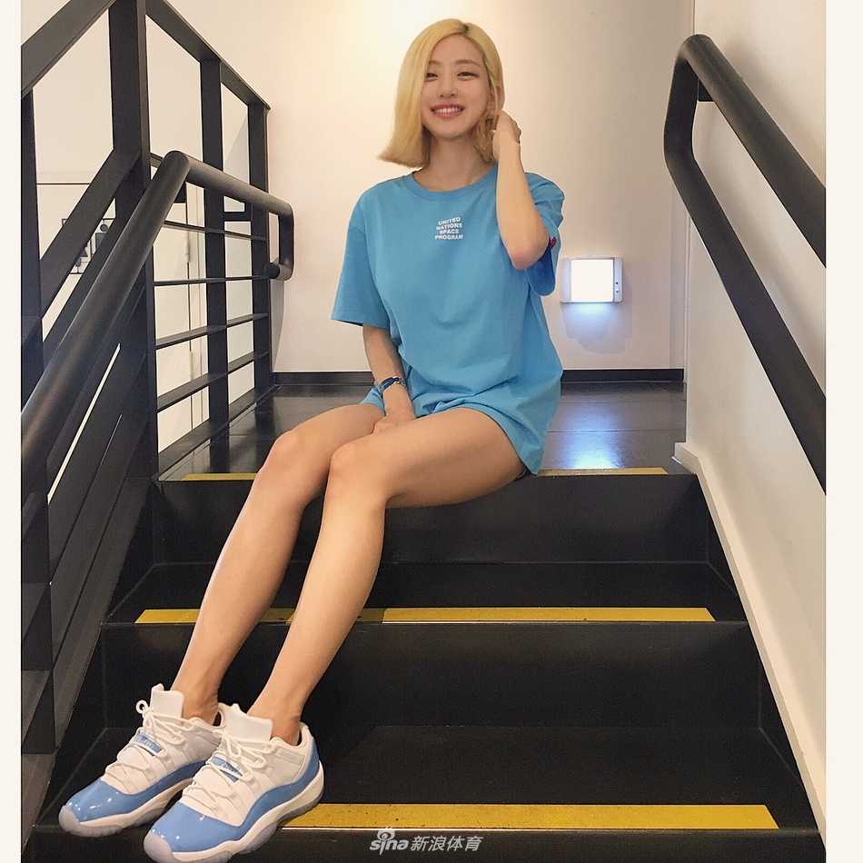 在一面巨大的鞋墙前，DJ Soda侧身站立，手里拎着一双金色的球鞋，墙上密密麻麻摆满了限量款球鞋，她脸上带着自信的微笑，好身材与满墙的潮鞋相得益彰。