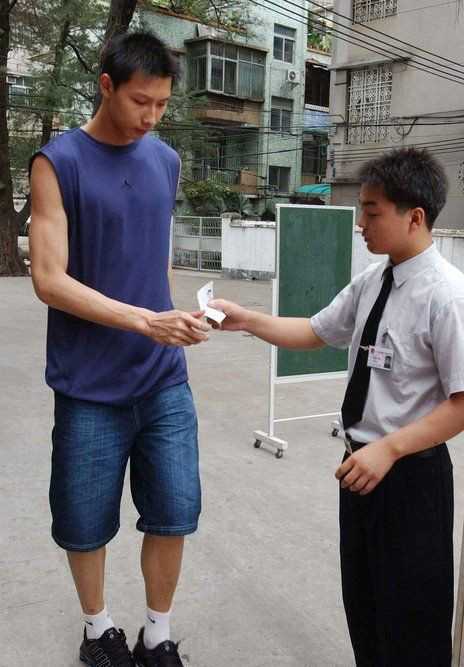 易建联戴着口罩，正在配合考场工作人员测量体温，他个子太高了，不得不深深弯腰，脸上带着一丝‘这关比打球难’的无奈笑意。