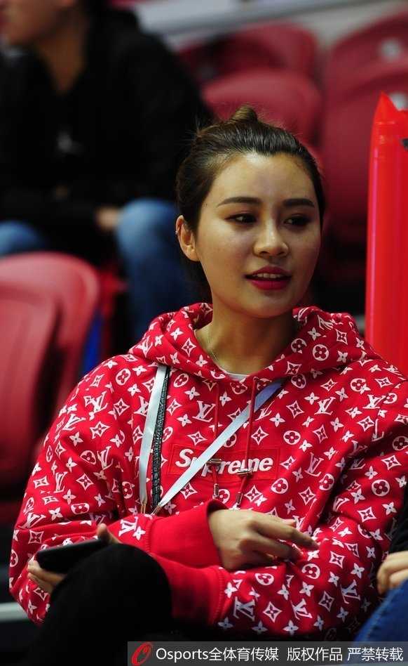 赛场边的温情一幕：李根妻子观看比赛时微微侧身，丸子头造型显得她青春洋溢，她正与友人分享观赛感受，心情似乎不错。