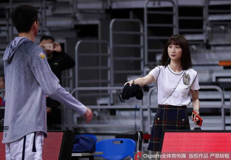 孙桐林的妻子端坐在篮架后方的家属区，眼神紧紧跟随着场内正在热身的丈夫，面带一丝紧张与期待，仿佛在用目光传递着无声的支持