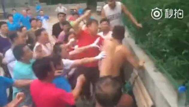 一名光着上身的年轻人在球场边被数名老人团团围住，手臂被拉扯，冲突一触即发，气氛紧张至极。