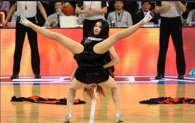 一位篮球宝贝在完成一字马动作后，低头微笑，眼神温柔而充满感染力，她身后的队友们还在尽情舞动，整个画面定格了活力与柔美的完美结合，让人感受到篮球宝贝的热情。