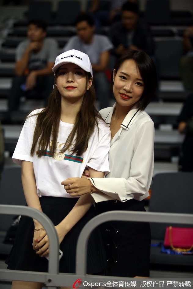 一位长发披肩的女球迷侧身望向场内，嘴角带着若有若无的笑意，精致的侧颜在球场灯光下格外引人注目。