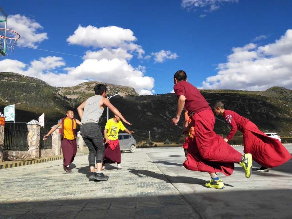 夕阳的余晖洒在简陋的水泥地球场上，给几位围在一起商讨战术的喇嘛镀上了一层温暖的金边。他们用手比划着，表情认真而放松，仿佛在进行一场神圣的仪式。