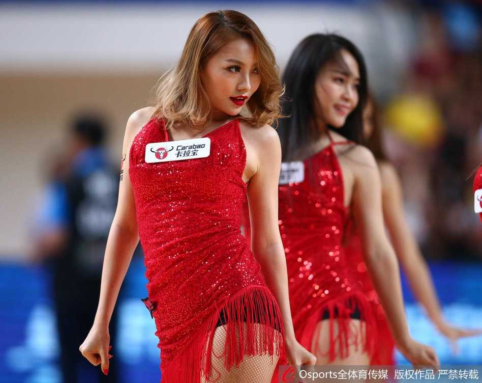 啦啦队员旋转瞬间，红裙如火焰跳动，活力四射，手中的花球在灯光下划出金色轨迹