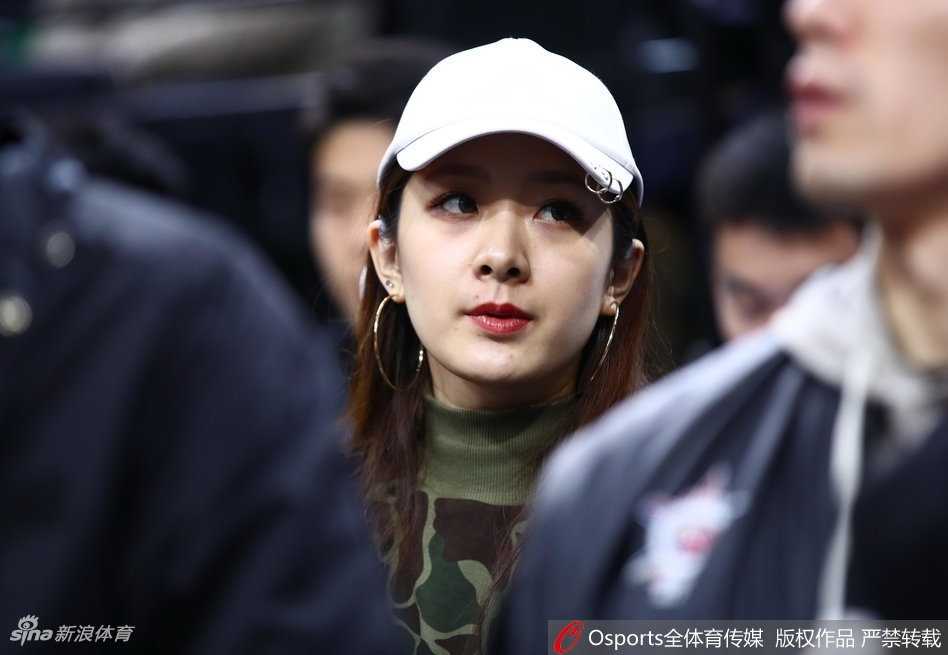 杨思雨在观众席上露出灿烂的笑容，眉眼弯弯，气质温婉大方。翟晓川则在一旁专注地看着她，眼神中充满爱意，背景是CBA全明星赛场的灯光与人群。