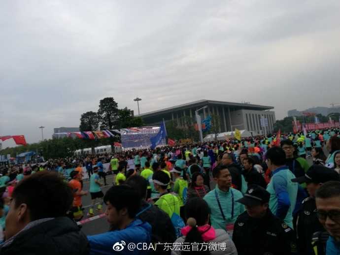 身着厚实外套的广东队明星球员易建联，在东莞清晨的微光中现身马拉松起跑点，他标志性的笑容如同暖阳，瞬间驱散了南国冬日的寒意，引来周围跑友惊喜的目光。