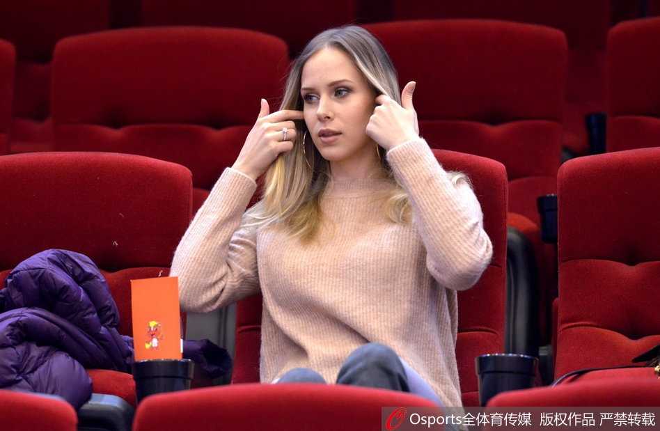 宝莲娜在观赛间隙低头查看手机，或许是在记录这场比赛的精彩瞬间，又或是在与无法到场的亲友分享此刻的喜悦，背景是模糊的球场和观众。