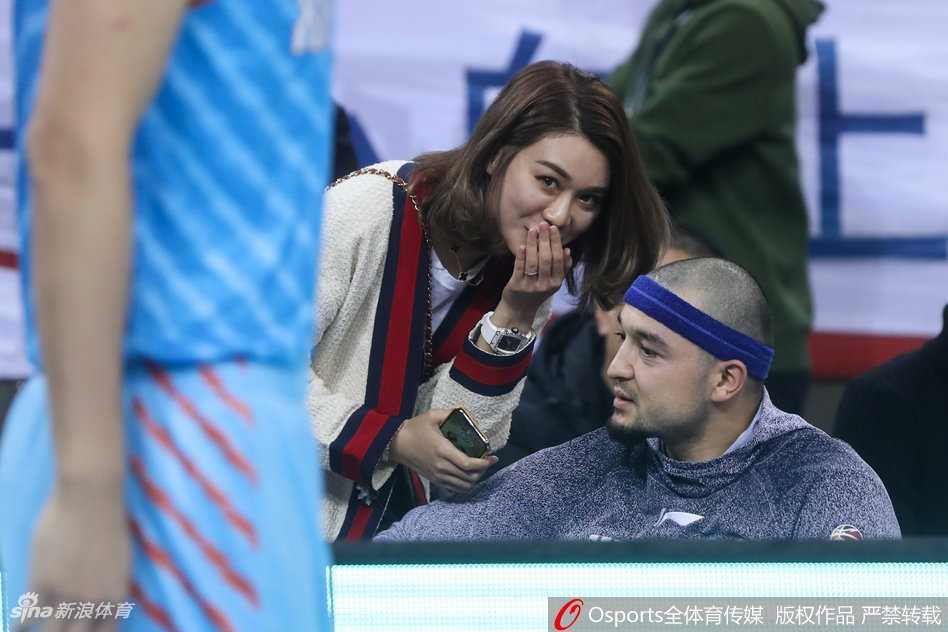 新疆队替补席后的看台上，李根妻子面带微笑为球队的精彩进球鼓掌，身边是热情的北京球迷，她显得优雅又得体。