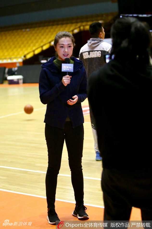 山东男篮的训练场上，一位高大的内线球员正持球背身单打，防守球员全力以赴，而在底线附近，美女记者半蹲着身子，以低角度抓拍着这次激烈的攻防对抗，神情极为投入。