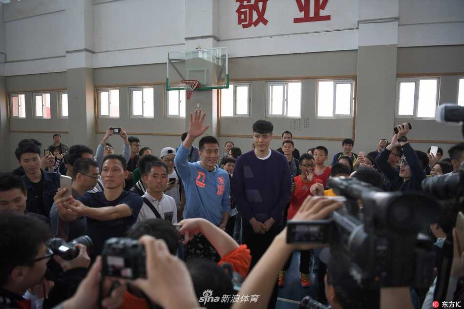 在投篮教学环节，贺天举化身为严厉的教练，亲自示范并纠正一位小球员的投篮姿势，周围的其他队员都在聚精会神地学习。