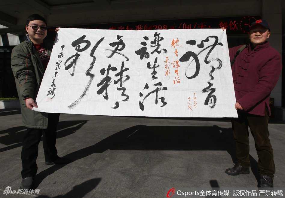 热情的球迷们紧紧跟随缓缓启动的大巴车，他们挥舞着手中的旗帜，用整齐划一的口号为心中的英雄送上最后一段路的陪伴。