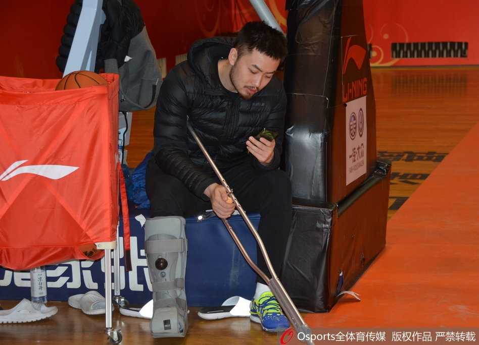 山东高速男篮赛前训练，受伤的队长睢冉拄着双拐，右脚穿着巨大的白色保护靴，独自坐在场边的椅子上，神情专注地看着远处正在热身的队友们。