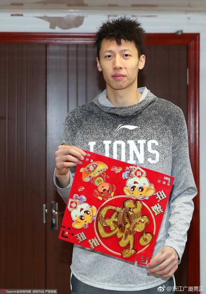 队长胡金秋手持火红福字，坚毅的眼神中透露出节日的温情，身后仿佛映照着黄龙体育馆的冠军旗帜