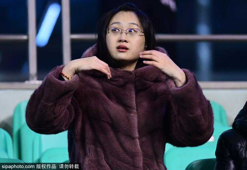 本溪体育馆入口处，一位身着棕色貂皮大衣的女球迷正在检票，她身后的背景是CBA联赛的巨幅海报，寒冷的空气中，她的身影显得格外引人注目，仿佛不是来看球，而是来参加一场冰雪中的时尚盛宴。