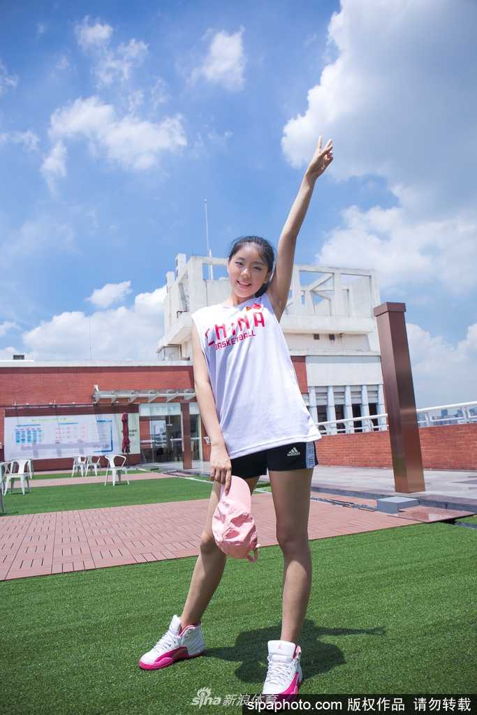 在室内影棚的柔和光线下，一位篮球宝贝身着粉色运动上衣，轻抚秀发，眼神温柔而坚定，展现出邻家女孩般的亲和力与赛场下的恬静气质。