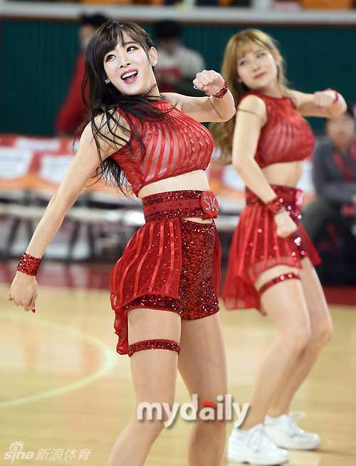 特写镜头下，这位啦啦队员单手叉腰，金色亮片抹胸在灯光下熠熠生辉，她微微侧身回眸，如瀑的长发遮住半边脸颊，眼神中透出自信而迷人的光彩，背景是虚化的看台人海。